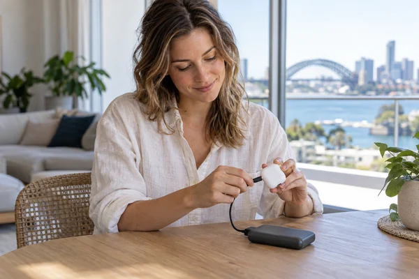 Adult woman connecting an earbud charging case to a portable power bank in an Australian-style home