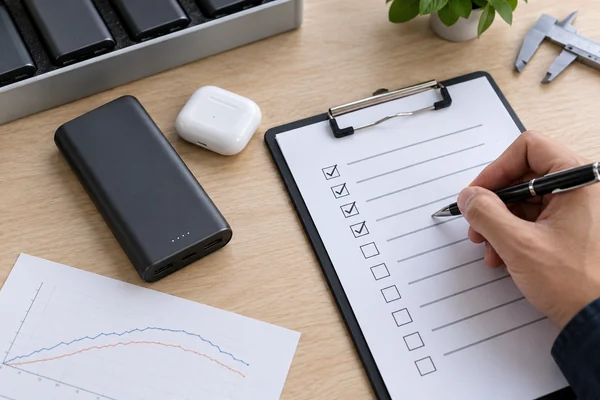 Illustrative OEM test checklist beside a power bank and earbud charging case