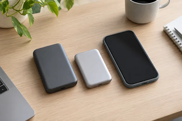Concept comparison of two unbranded power bank sizes beside a smartphone in a protective case.
